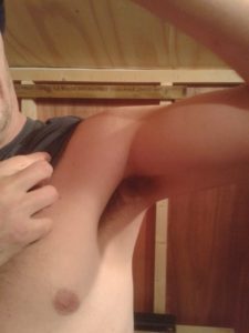A person lifts their arm to reveal their armpit, displaying body hair—capturing an intimate moment indoors with wooden...