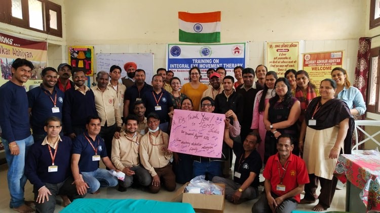 A large group of people pose indoors, some standing and some kneeling, holding a pink thank you poster. An Indian flag...