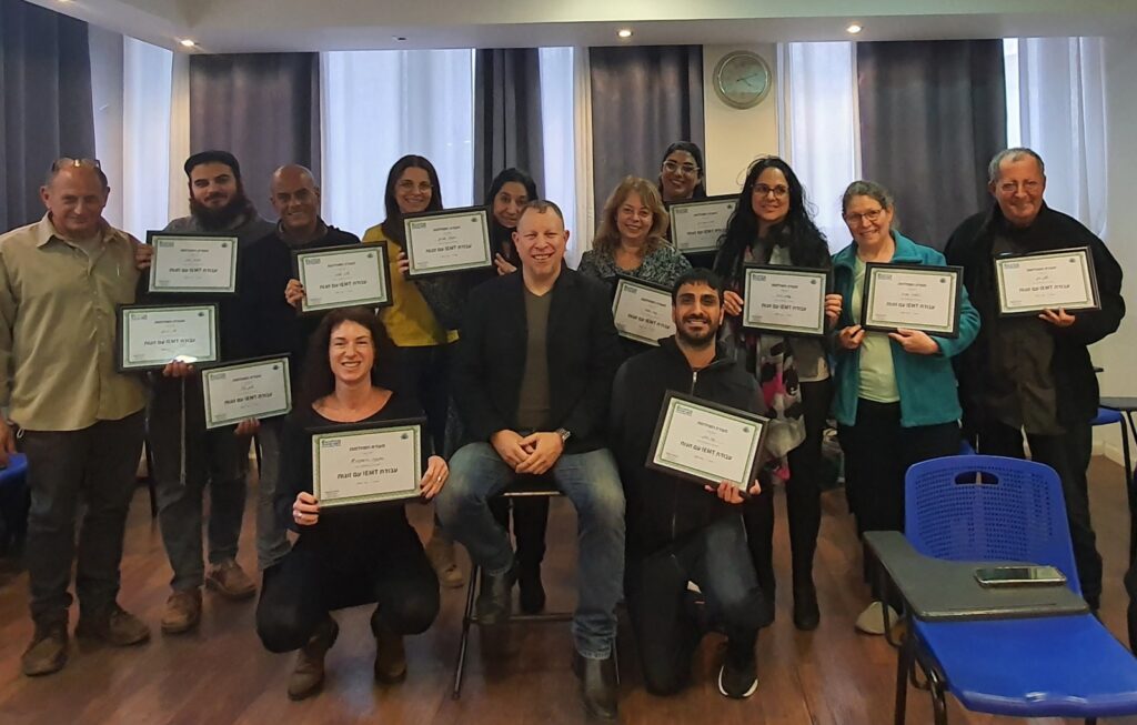 A group of thirteen people pose indoors, smiling and holding certificates after completing an EMDR trauma workshop. Most...