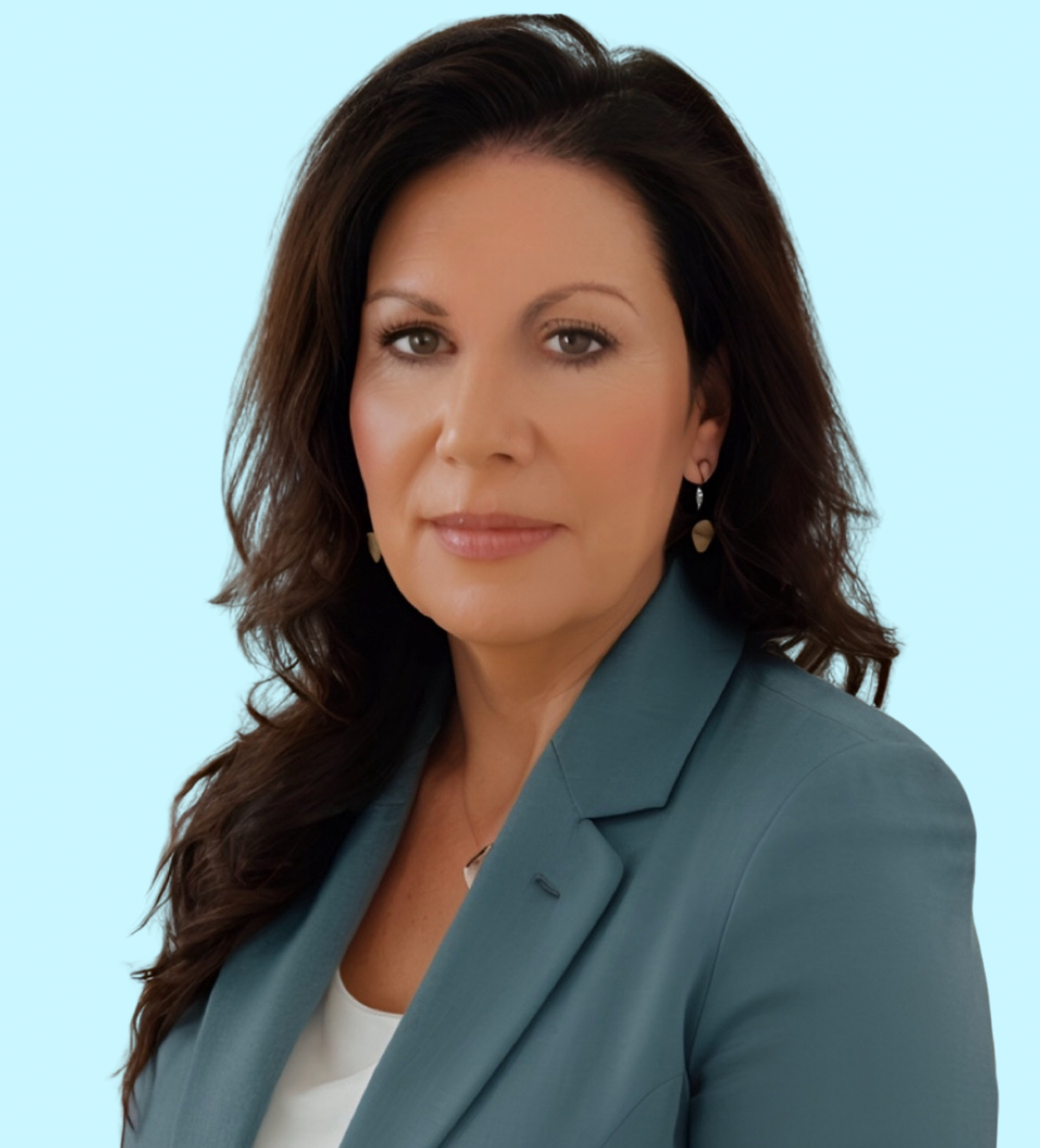 A woman with long dark hair wearing a teal blazer and white top poses against a light blue background, looking directly...